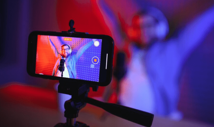 A picture showing a video blogger filming content on a mobile phone. The blogger is employing the use of mobile streaming improvement ideas like good lighting and camera angles to boost the quality of the content.